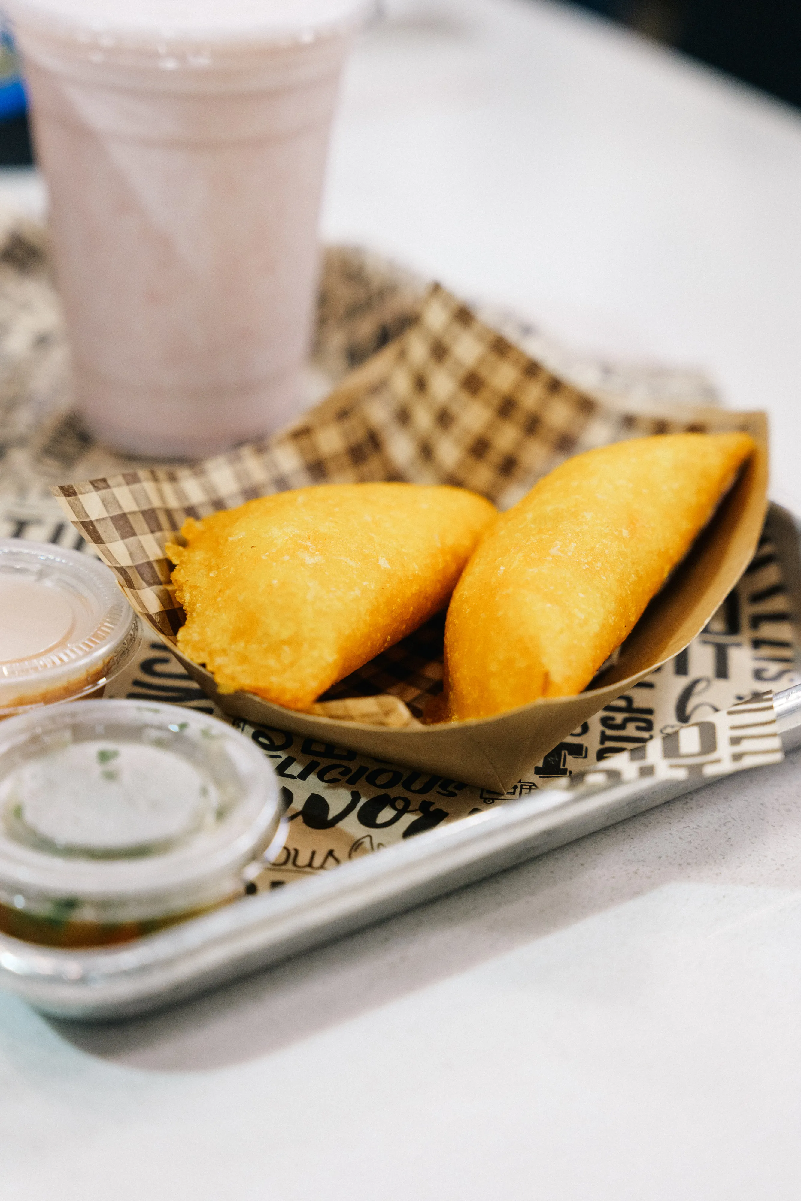 Two golden Colombian empanadas in a paper boat with dipping sauce