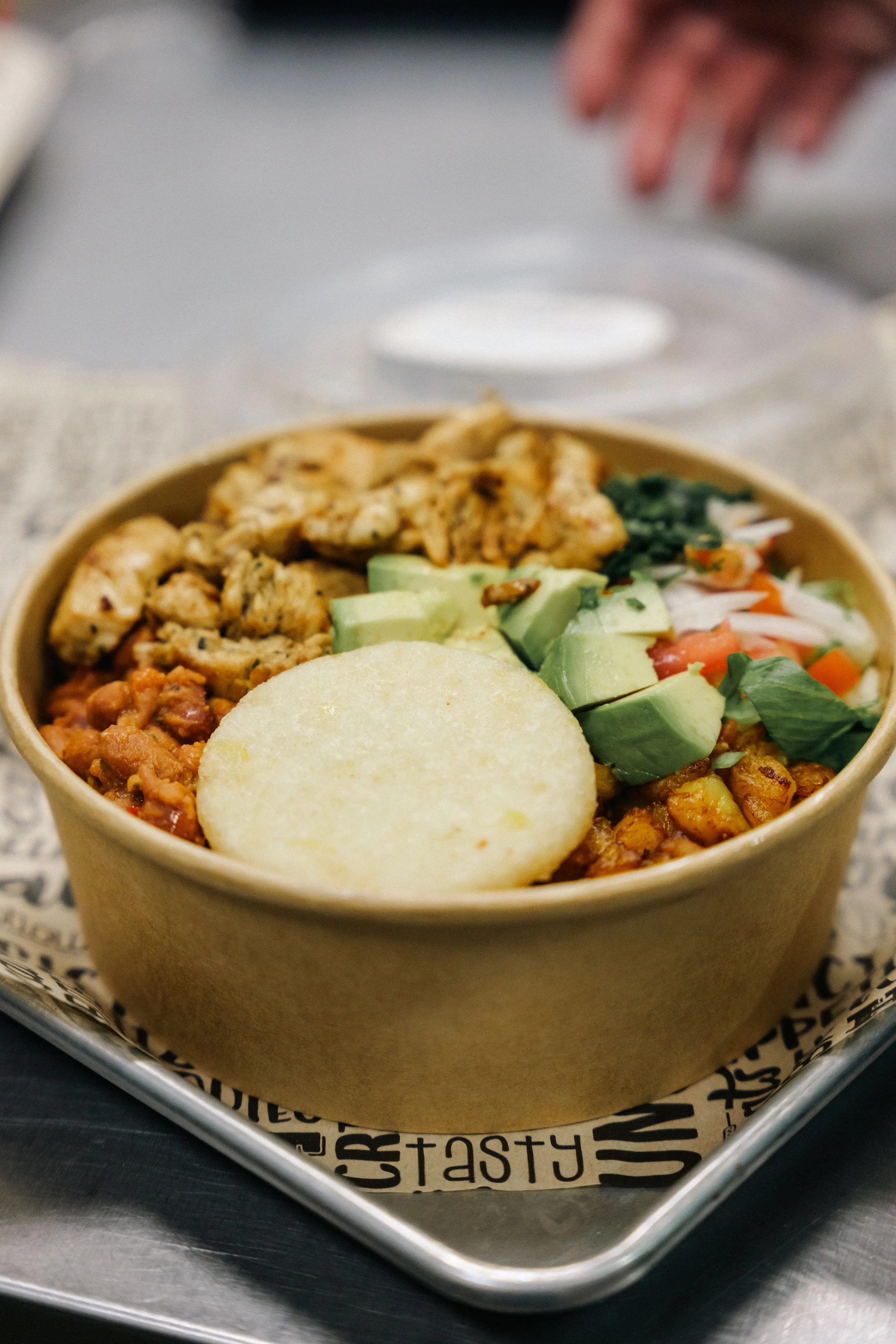 A Pardito's bowl of rice, chicken, avocado, arepa and fresh vegetables